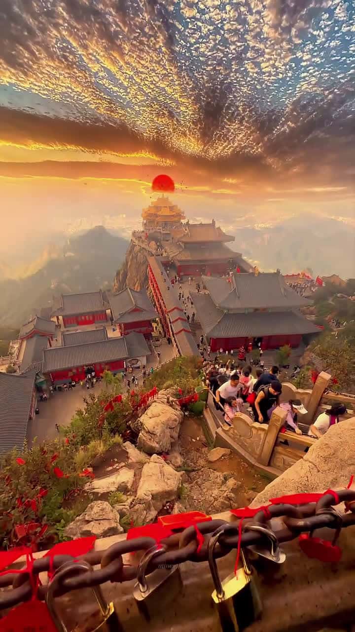 Cover for This breathtaking shot captures a panoramic view from Mount Tai (Tai Shan), one of China's Five Great Mountains and a UNESCO World Heritage Site. The scene is steeped in cultural, spiritual, and natural beauty.A long stone stairway winds up the mountain, filled with people making the sacred pilgrimage to the Golden Summit, where traditional Chinese temple structures with ornate rooftops sit perched on the cliffs. The architecture features classic red and gray tones, symbolizing strength and re